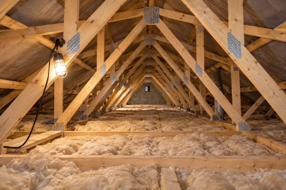 Fermettes industrielles en W dans un comble de pavillon, bois clairs et connecteurs métalliques