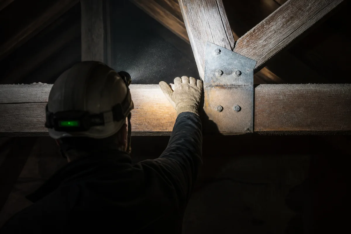 Charpentier inspectant une panne en bois dans un comble avec une lampe frontale