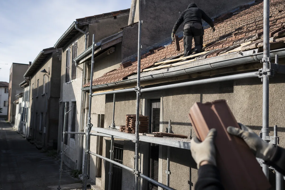 Chantier de rénovation de toiture sur une maison de mineurs du bassin stéphanois, échafaudage monté en rue étroite et tuiles mécaniques neuves