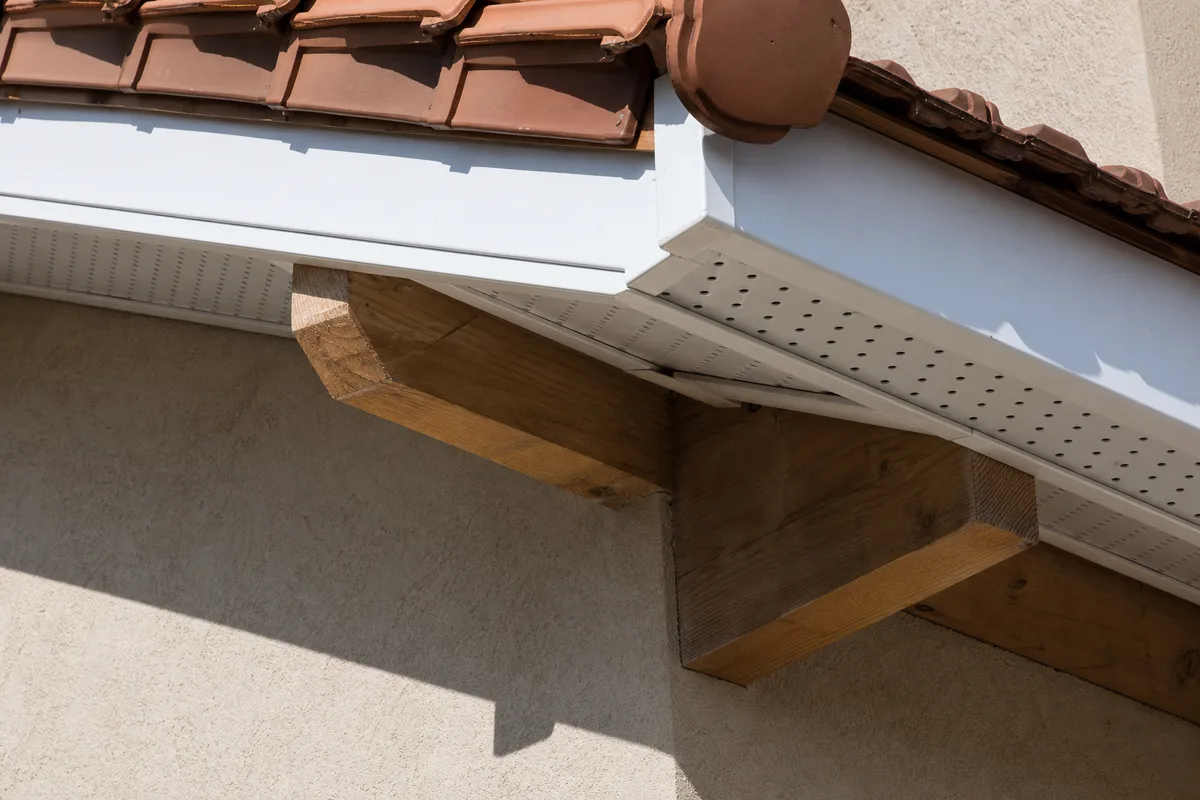 Détail d’un débord de toit rénové, planche de rive et sous-face en PVC blanc sur une maison de bourg